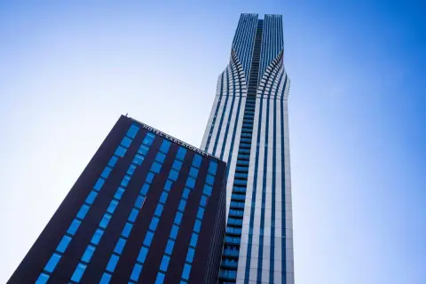 Två moderna skyskrapor mot en blå himmel. Den ena, med texten HOTEL KARLATORNET, har mörka fasader och blå fönster. Den andra är hög och smal med vita och blå vertikala linjer.
