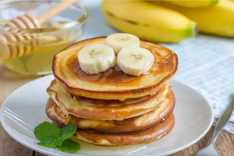 En stapel gyllene bananpannkakor toppas med bananskivor och ringlad honung. Ett enkelt bananpannkaka recept för en härlig frukost.