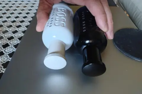 Dwie butelki perfum Hugo Boss, jedna biała męska, druga czarna, leżą obok siebie.
