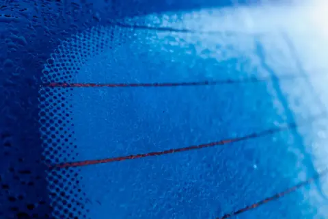 Gotas de agua sobre los **filamentos transversales de la luneta trasera** de un coche, creando un patrón abstracto azul.