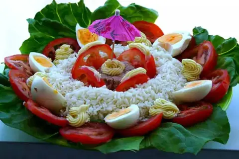 Salade de riz thon festive, garnie d'œufs durs, tomates, mayonnaise et d'un petit parasol rose. Un délice coloré !