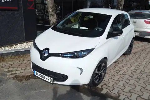 Białe Renault Zoe stoi zaparkowane na chodniku z kostki brukowej.
