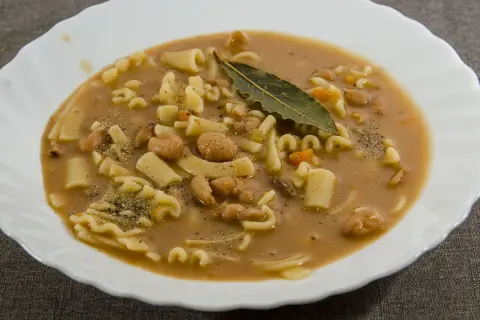 Un piatto fumante di pasta e fagioli, con pasta corta, fagioli borlotti, carote e una foglia di alloro.