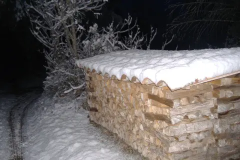 Une pile de bois peuplier chauffage sous la neige, prête pour l'hiver. Les branches enneigées d'un arbre se dressent à gauche.