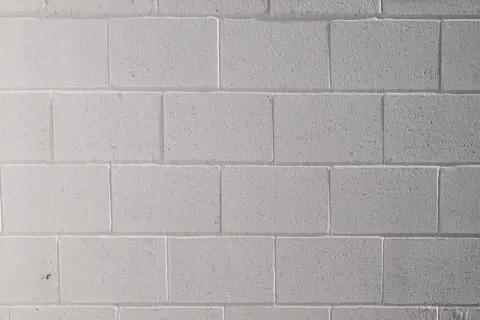 Mur de parpaings blancs, fraîchement peints au pistolet. La texture rugueuse des blocs est visible sous la couche de peinture uniforme.