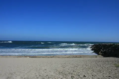 Arena dorada, mar azul y olas rompiendo en esta playa marosa. Gaviotas pasean tranquilas.