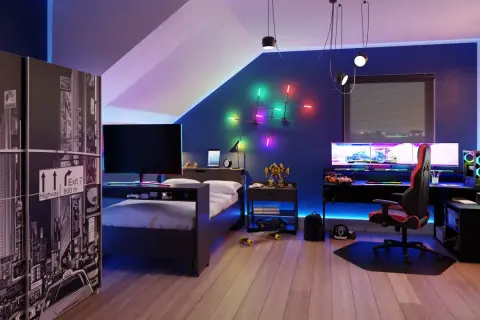 Nowoczesny pokój gamingowy na poddaszu z łóżkiem, biurkiem z potrójnym monitorem i kolorowym oświetleniem LED.