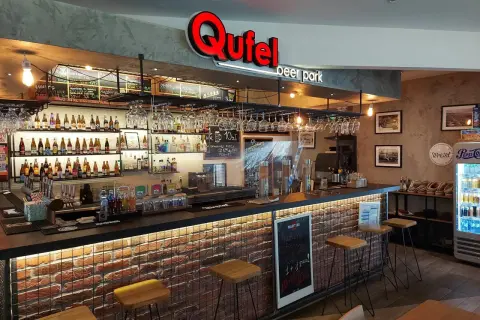 Wnętrze Qufel beer park z barem, butelkami piwa i menu.