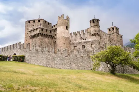 Imponente castello medievale, uno dei borghi Valle d'Aosta più suggestivi, con torri merlate e mura in pietra su un prato verde.