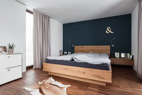 Modernes schlafzimmer blau holz mit einem Doppelbett aus hellem Holz, dunkler Wand und Teppich.
