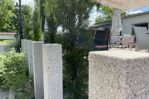 Granit-Palisaden setzen einen eleganten Akzent vor grüner Bepflanzung und laden zum Verweilen auf der Terrasse ein.