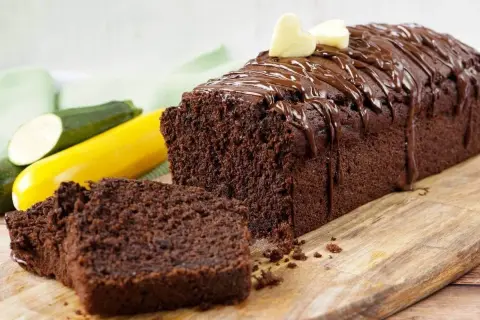 Saftiger Zucchini Schoko Kuchen, mit Schokoladenglasur und Herz-Dekoration, daneben Zucchini und gelbe Zucchini.