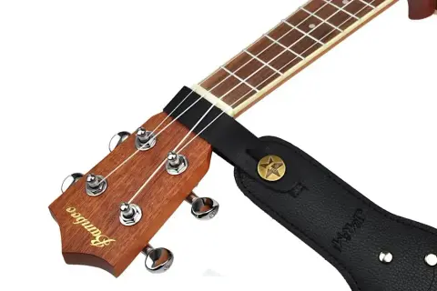 Czarny pasek do gitary zaczepiony na gryfie ukulele. Pokazuje, jak zacząć grać, gdy masz już zamontowany pasek.