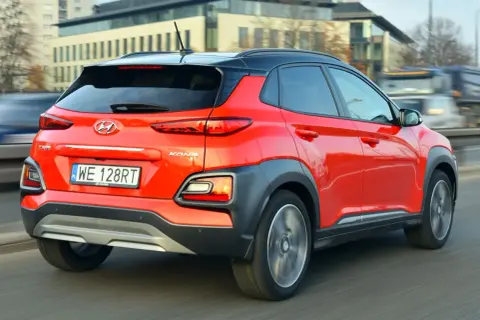 Czerwony Hyundai Kona 2025 z czarnym dachem pędzi po drodze, ukazując swoje nowoczesne tylne światła i masywne nadkola.