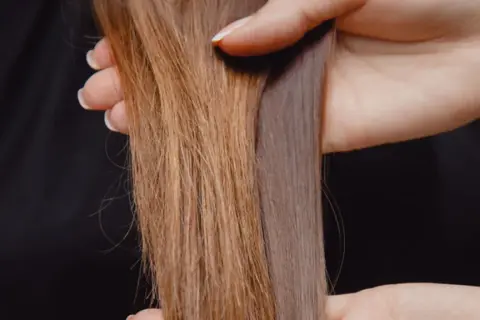 Hände halten zwei Strähnen Haar, eine glänzend, die andere matt und glanzlos.