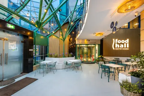 Nowoczesna strefa gastronomiczna "food hall Krzywy Domek Sopot" z zielonymi meblami i oświetleniem.