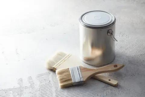Metalowa puszka z farbą i dwa pędzle na szarej, chropowatej powierzchni.