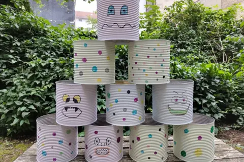 Kreatives Recycling mit Kindern: Dosen-Monster-Turm im Garten. Bunte Punkte und lustige Gesichter machen aus alten Konserven ein Spiel.
