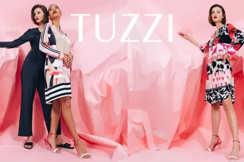Eleganckie kobiety prezentują modne kreacje marki TUZZI na tle różowych, pofałdowanych tkanin.