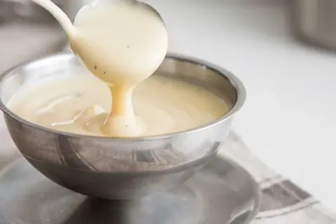 Krämig vaniljsås hälls från en slev i en skål. Perfekt för ditt vaniljsås recept.