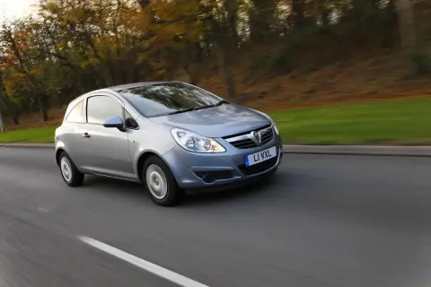 Srebrny Opel Corsa D 1.2 benzyna w ruchu, z rozmytym tłem jesiennego lasu.