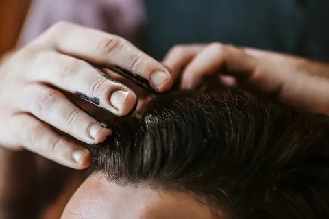 Main d'un coiffeur appliquant du gel ou de la cire sur les cheveux d'un client pour un coiffage parfait.