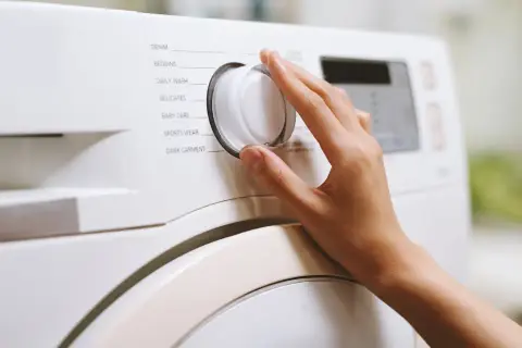 Dłoń kręci pokrętłem pralki, wybierając program "Bedding". Zastanawiasz się, w jakiej temperaturze prać pościel z kory? Sprawdź instrukcję pralki.