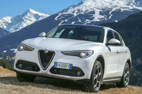 Białe Alfa Romeo Stelvio na tle ośnieżonych gór. Wiele pozytywnych alfa romeo stelvio opinie potwierdza jego wszechstronność.