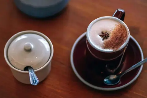 En kopp krämigt chai te med stjärnanis och kanel, redo för ett mysigt chai te recept. Bredvid står en sockerskål med sked.
