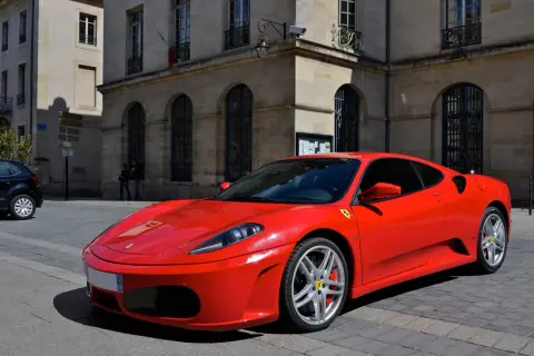 Czerwone Ferrari F430 na brukowanej ulicy przed kamienicą. Zastanawiasz się, ile kosztuje Ferrari? To marzenie wielu kierowców.