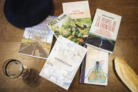 Un béret, un verre de vin, une baguette et plusieurs livres sur la France, dont "Voyages en France" et "La Diagonale du vide", parfaits pour un récit de voyage.