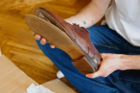 Une personne examine une chaussure en cuir marron, montrant l'usure de la semelle.
