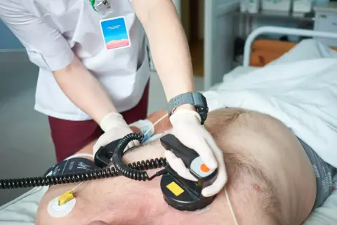 Ratownik medyczny wykonuje kardiowersję pacjentowi leżącemu w łóżku szpitalnym.
