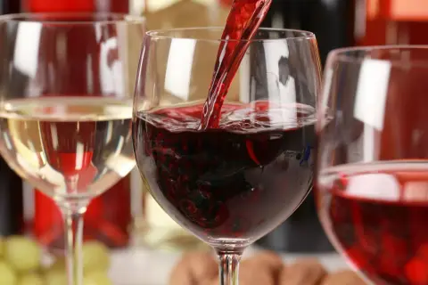 Czerwone wino nalewane do kieliszka, obok białe wino i butelki. Zastanawiasz się, ile kalorii ma wino?