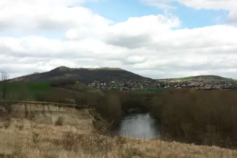 Vue panoramique d'une rivière sinueuse bordée d'arbres, avec une falaise de malmouche en contrebas et un village niché sur une colline verdoyante.