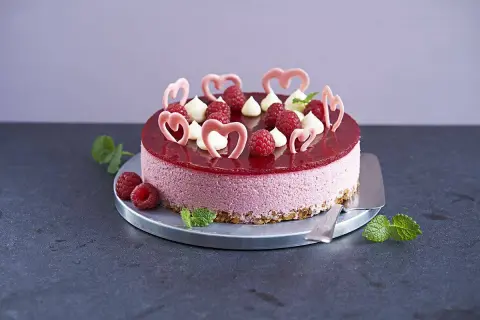 En vacker hallonmousse tårta med färska hallon, vita gräddtoppar och rosa hjärtdekorationer. Perfekt för ett speciellt tillfälle!