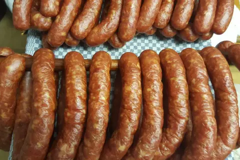 Gotowy przepis na kiełbasę swojską 5 kg. Wędliny wiszą na drewnianych kijach, gotowe do dalszej obróbki.