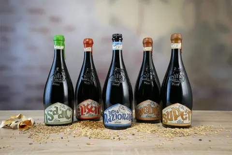 Cinque bottiglie di birra Baladin, tra le migliori birre artigianali italiane, disposte su un letto di cereali.