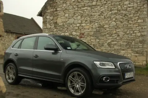 Szary Audi Q5 Quattro zaparkowany przy kamiennym budynku.
