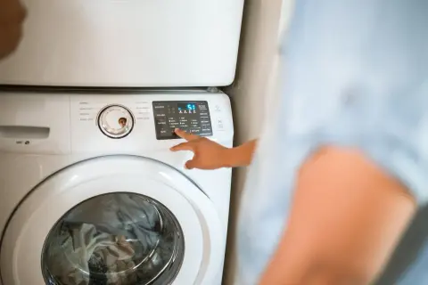 Mano che seleziona "Warm" sul pannello di una lavatrice, per capire quanto consuma una lavatrice a 40 gradi.