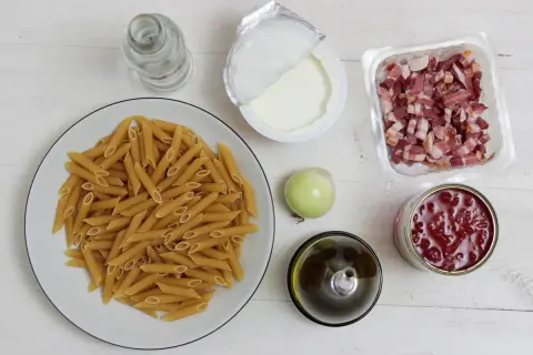 Penne, boczek, śmietana, cebula, oliwa, pomidory z puszki na białym tle.
