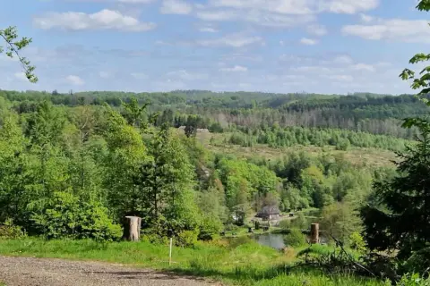 Grüne Hügel und Wälder säumen die Eckenhagen Route. Ein kleiner Teich mit einem Haus liegt eingebettet in der Landschaft.