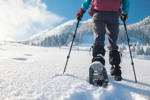 Randonnée en raquettes dans un paysage enneigé. Une personne avance dans la poudreuse, bâtons à la main, profitant des sports neige.