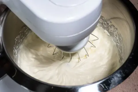Mieszadło robota kuchennego ubija puszysty krem z ricotty do ciasta.