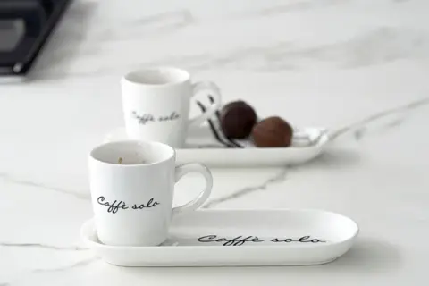 Eleganckie filiżanki z napisem "Caffè solo" i czekoladki na talerzykach. Idealny sposób, jak podawać kawę gościom.