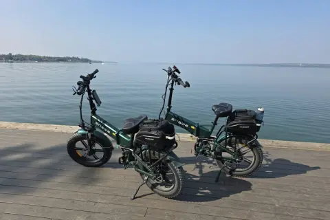 Dwa zielone rowery elektryczne z sakwami, gotowe na wyprawę z zasięgiem 200 km nad spokojną wodą.