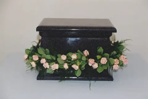 Czarna, kamienna urna ozdobiona girlandą z różowych różyczek i zieleni. Piękne kwiaty na trumnę, symbolizujące pamięć i miłość.