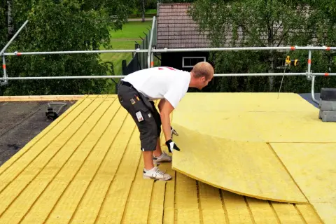 Pracownik układa płyty izolacyjne do ocieplenia dachu płaskiego.