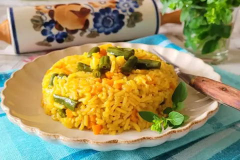 Ryż z curry, marchewką i fasolką szparagową na talerzu, ozdobiony ziołami.