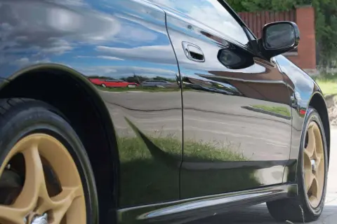Błyszczące czarne uni auto z złotymi felgami odbija niebo i otoczenie.